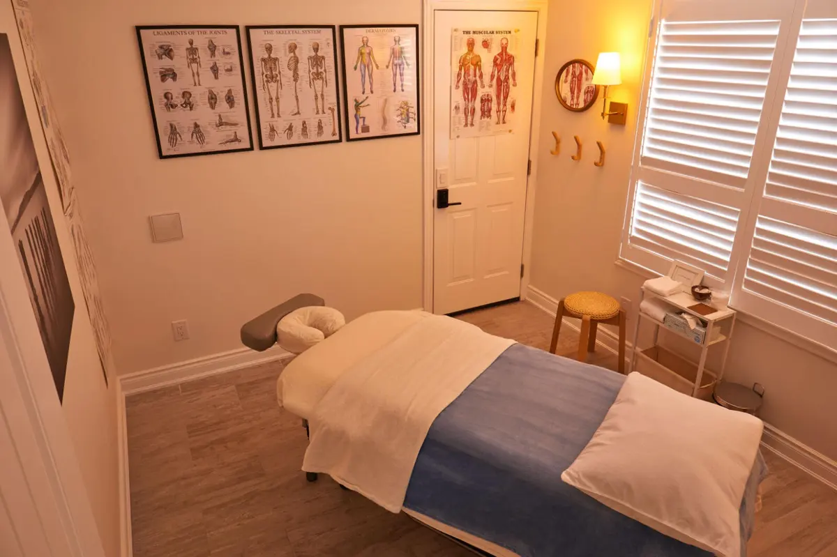 Michèle's treatment room: a massage table with blue and white linens, anatomy charts on the wall and a warm lamp by the window